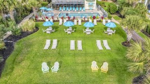 A poolside area with lounge chairs and umbrellas, a pool, and a building with a glass facade. - Oceanfront Penthouse, Amazing Views, Walk to Conv Center, Attractions & Dining (Myrtle Beach)