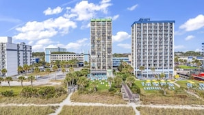 A high-rise hotel with multiple floors, a parking garage, and a landscaped area with pathways and palm trees. - Oceanfront Penthouse, Amazing Views, Walk to Conv Center, Attractions & Dining (Myrtle Beach)
