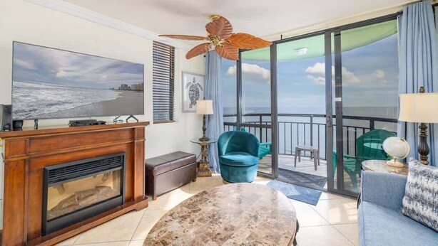 A spacious living room with a fireplace, a television, and a large window offering a view of the ocean. - Oceanfront Penthouse, Amazing Views, Walk to Conv Center, Attractions & Dining (Myrtle Beach)