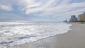 A beach with waves, a clear sky, and buildings in the background. - Oceanfront Penthouse, Amazing Views, Walk to Conv Center, Attractions & Dining (Myrtle Beach)