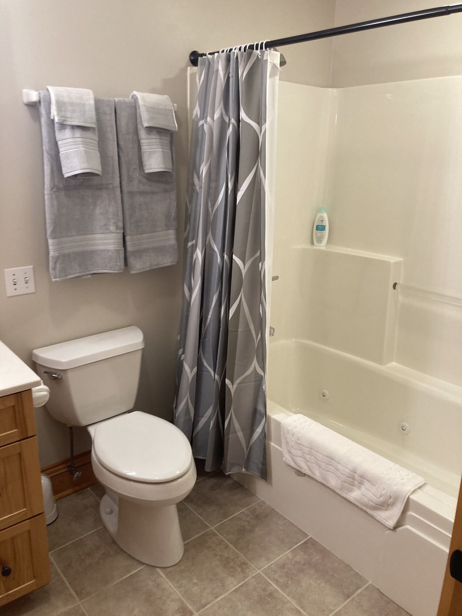 A bathroom with a toilet, a shower with a glass door, and a bathtub. There are two towels hanging on the wall and a bottle of shampoo on the bathtub shelf.