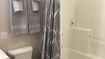 A bathroom with a toilet, a shower with a glass door, and a bathtub. There are two towels hanging on the wall and a bottle of shampoo on the bathtub shelf.