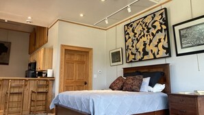 Een slaapkamer met een bed, houten kasten, een keukenhoek en kunstwerken aan de wanden.