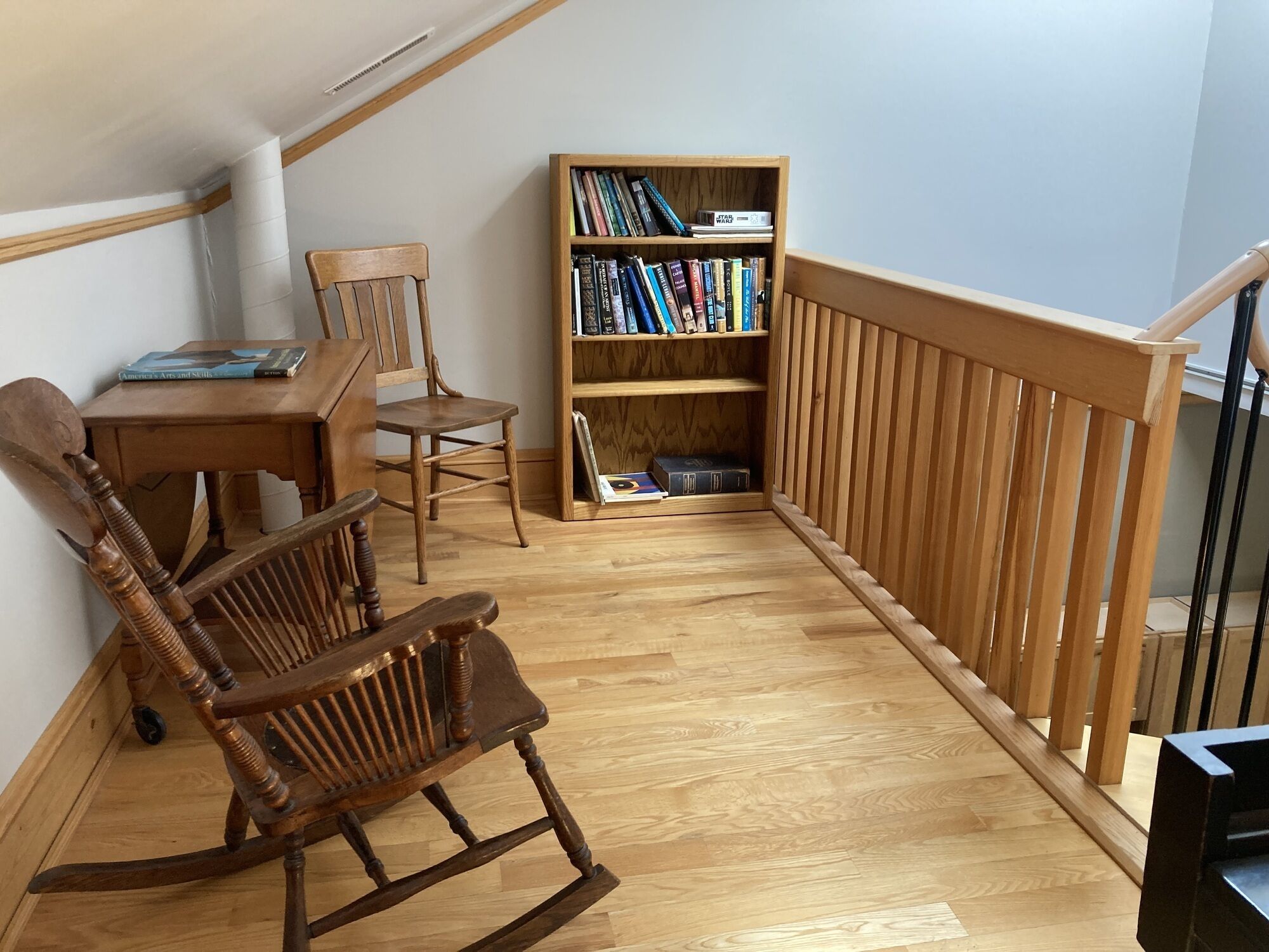 A cozy reading nook with a wooden rocking chair, a small table, and a bookshelf filled with books.