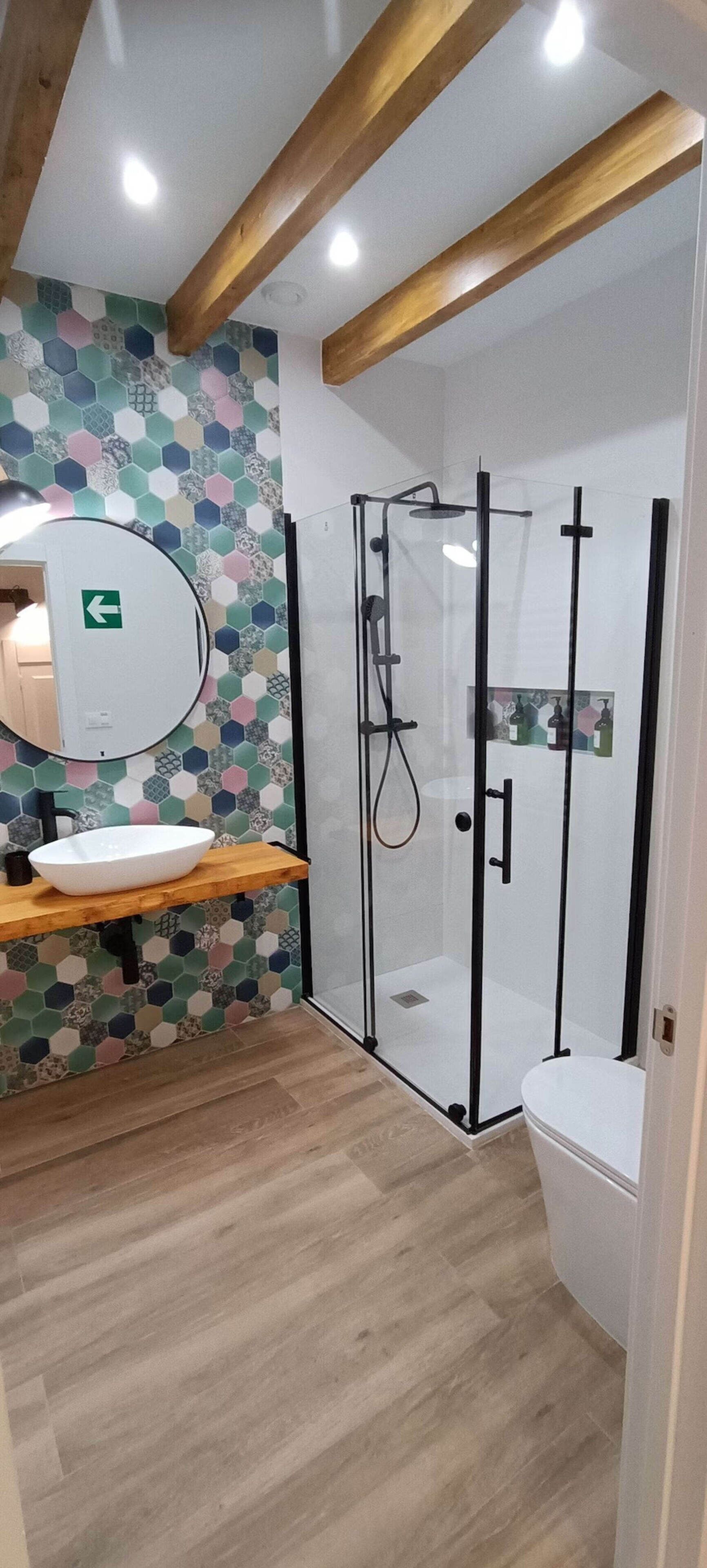 Un baño moderno con tocador de madera, espejo redondo, cabina de ducha con mampara de vidrio y pared con azulejos.