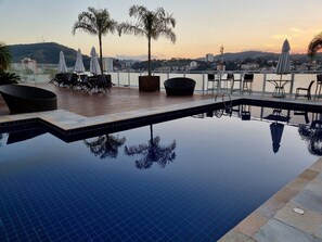 A rooftop infinity pool with lounge chairs and umbrellas, surrounded by a cityscape view. - Mansao no centro São Roque  (Sao Roque)