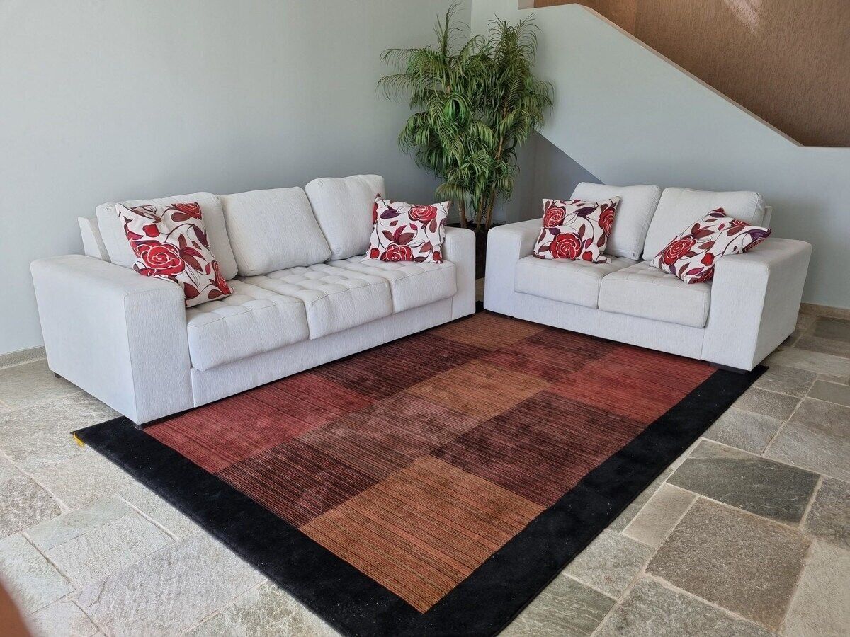 Un salon avec deux canapés blancs, un grand tapis à motifs et une plante en pot.