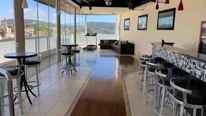 Une pièce spacieuse avec un long plancher en bois, un coin bar doté de tabourets et un espace salon avec un canapé et des fauteuils.