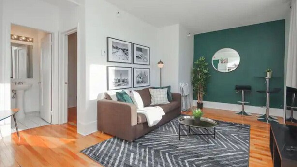 A living room with a brown sofa, a coffee table, a black rug, and framed pictures on the wall.