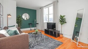 A modern living room with a green accent wall, a sofa, a coffee table, a TV, and a large mirror.
