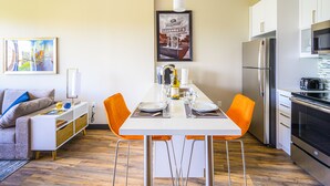 A modern kitchen with white cabinets, stainless steel appliances, and a dining area with orange chairs. - Revisn Executive Downtown Raleigh Apartment (Raleigh)