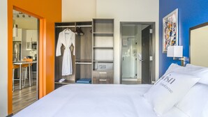 A hotel room with a bed, a robe hanging, a shower, and a view of the kitchen. - Revisn Executive Downtown Raleigh Apartment (Raleigh)