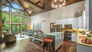 A spacious kitchen with a large island, wooden flooring, and a view of the outdoors. - Luxury Mountain Lodge • 4BR • Pool Table + PS5 • Fireplace • Views (McGaheysville)