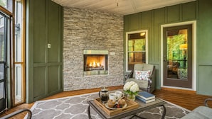 A cozy room with a stone fireplace, a comfortable chair, a coffee table with a tray of muffins, and a view of the outdoors. - Luxury Mountain Lodge • 4BR • Pool Table + PS5 • Fireplace • Views (McGaheysville)