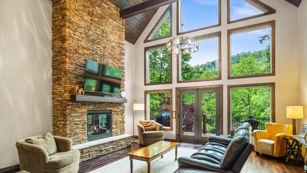 A spacious living room with a stone fireplace, large windows, and a high ceiling. - Luxury Mountain Lodge • 4BR • Pool Table + PS5 • Fireplace • Views (McGaheysville)