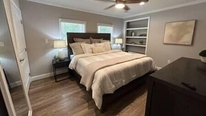 Een slaapkamer met een bed, nachtkastjes, een bureau, een plafondventilator en een raam.