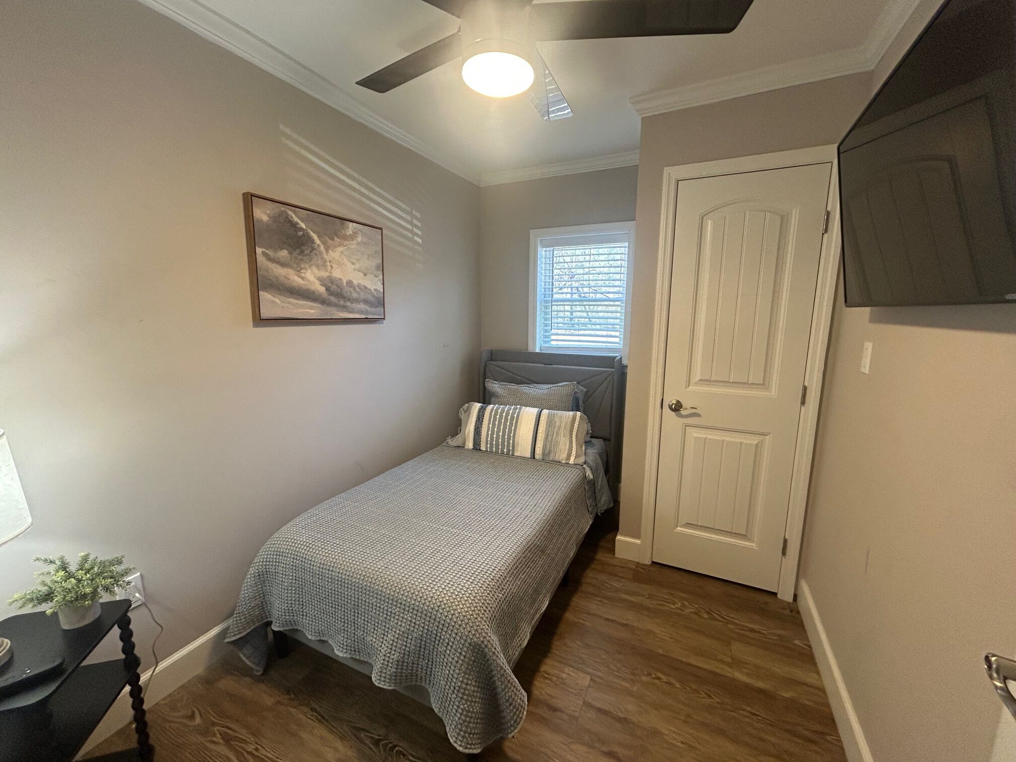 A small bedroom with a bed, a ceiling fan, a window with blinds, and a door.
