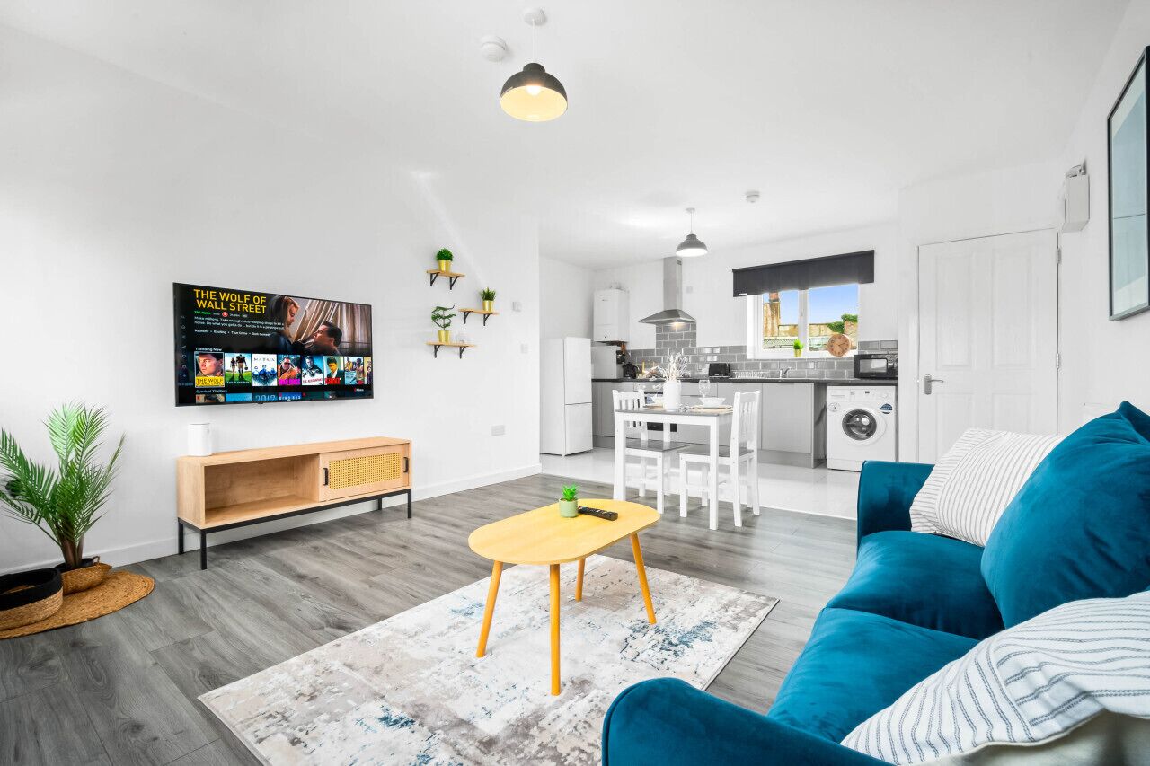 Een moderne woonkamer met een blauwe bank, een houten salontafel en een aan de muur bevestigde televisie.