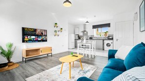 Ein modernes Wohnzimmer mit einem blauen Sofa, einem Holztisch und einem an der Wand befestigten Fernseher.