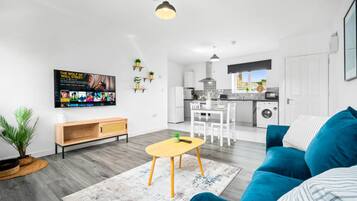 Een moderne woonkamer met een blauwe bank, een houten salontafel en een aan de muur bevestigde televisie.