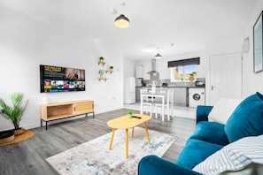 Ein modernes Wohnzimmer mit einem blauen Sofa, einem Holztisch und einem an der Wand befestigten Fernseher.