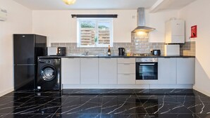Une cuisine moderne dotée d’un plan de travail en marbre noir, d’un lave-linge encastré, d’une cuisinière et d’une fenêtre donnant sur un paysage verdoyant.