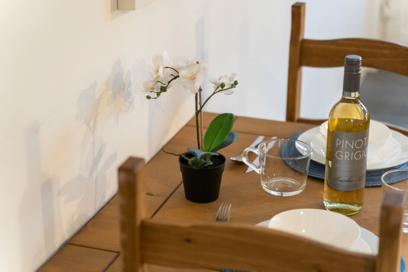 Een eettafel met een fles Pinot Grigio, een kleine pot met een plant, een glas en een vork.