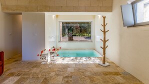 A bathroom with a stone floor, a bathtub, a window with a view of greenery, and a wooden decor piece.
