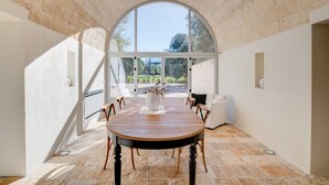 A dining area with a round table, chairs, and a view through a large arched window.