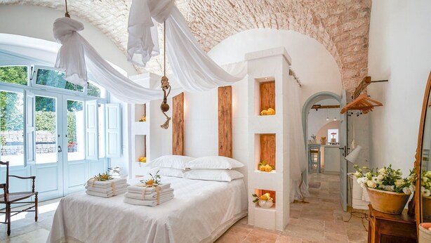 A bedroom with a large bed, a wooden wardrobe, and a window with a view of greenery.