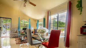 A modern living room with a glass dining table, a red chair, and a ceiling fan. - Casia Villa (Montego Bay)
