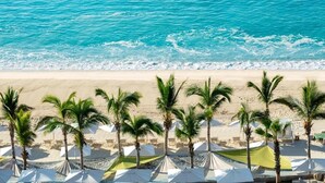 Una playa con sombrillas blancas y palmeras.