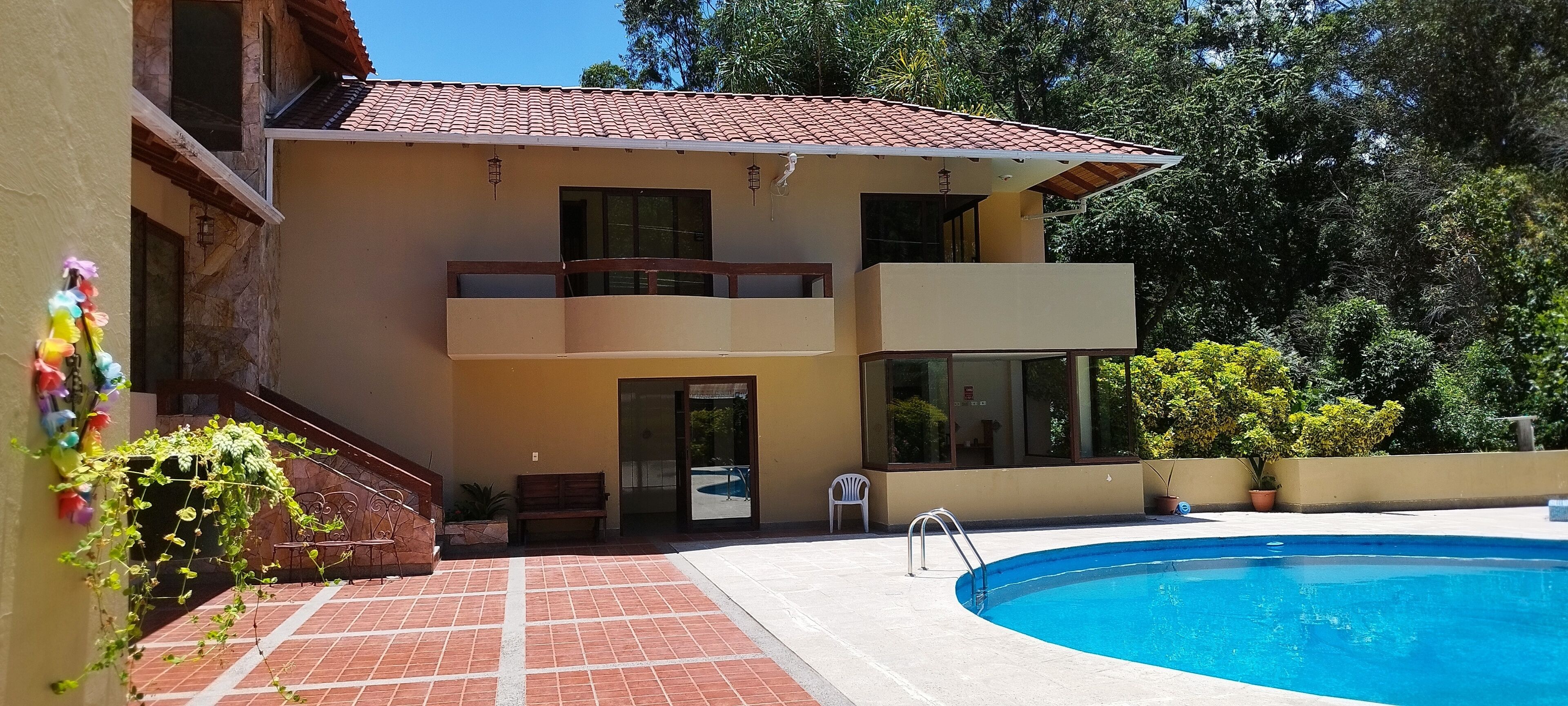 Un edificio de dos pisos con piscina, un balcón y una escalera que conduce a la entrada.