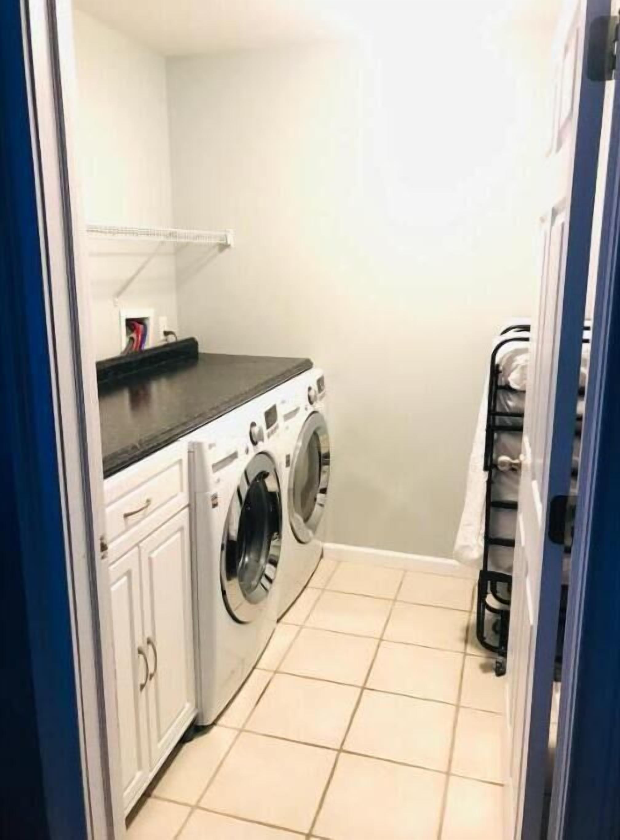 A laundry room with two front-loading washing machines, a drying rack, and a shelf with a few items.