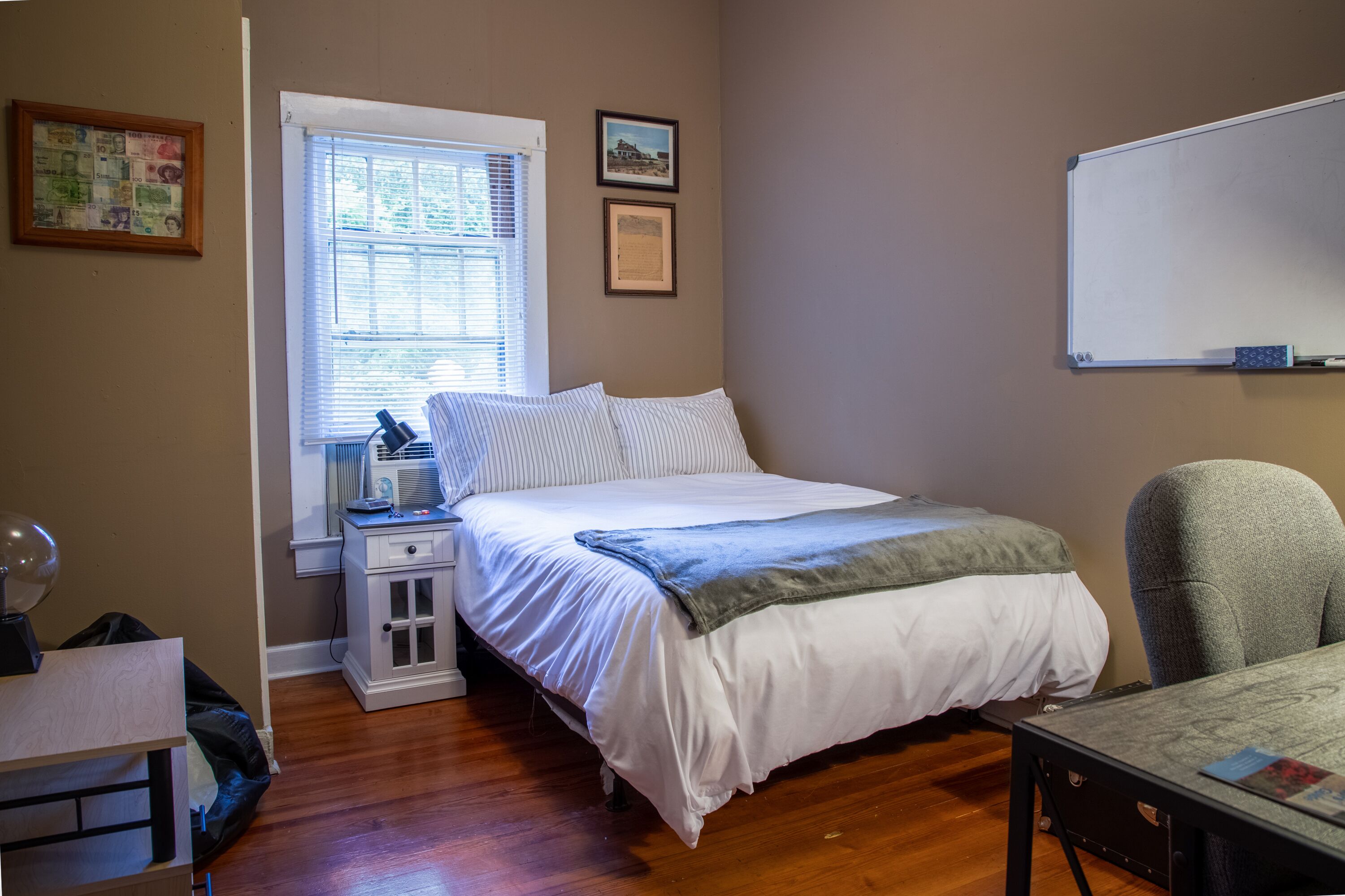 A bedroom with a bed, bedside table, chair, and a window with blinds.