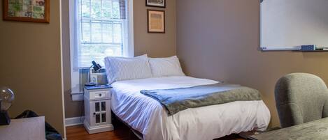 A bedroom with a bed, bedside table, chair, and a window with blinds.