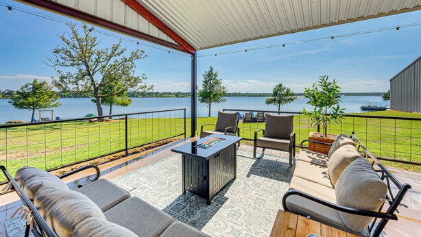 Eine überdachte Terrasse mit Gartenmöbeln, einer Feuerstelle und Blick auf den See.