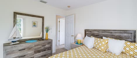 A bedroom with a bed, dresser, and a door leading to another room.