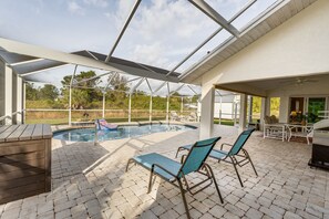 A covered outdoor area with a pool, lounge chairs, and a barbecue grill.