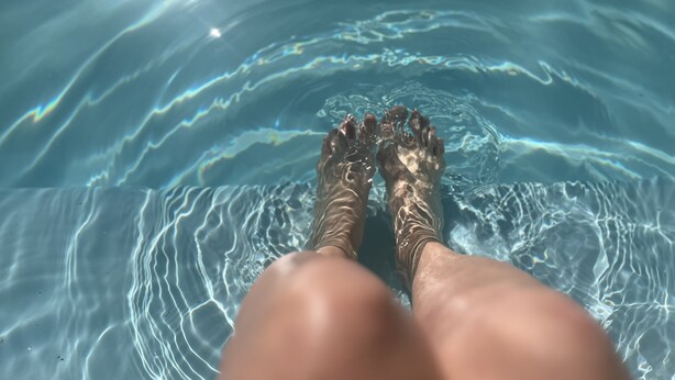 Piernas de una persona sumergidas en agua cristalina, con visibles ondulaciones y reflejos.