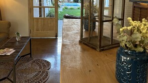 Una habitación con piso de madera, una puerta de vidrio que da a una piscina, un jarrón azul con flores y lámparas de mimbre.
