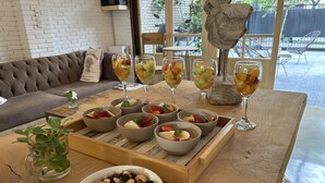 Una mesa de madera con fruteros, vasos de ponche de frutas, un bol de nueces y una planta en maceta.