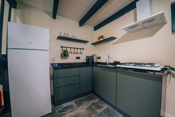 Une cuisine avec un réfrigérateur blanc, des meubles de rangement sombres, une cuisinière à gaz et un plan de travail noir.