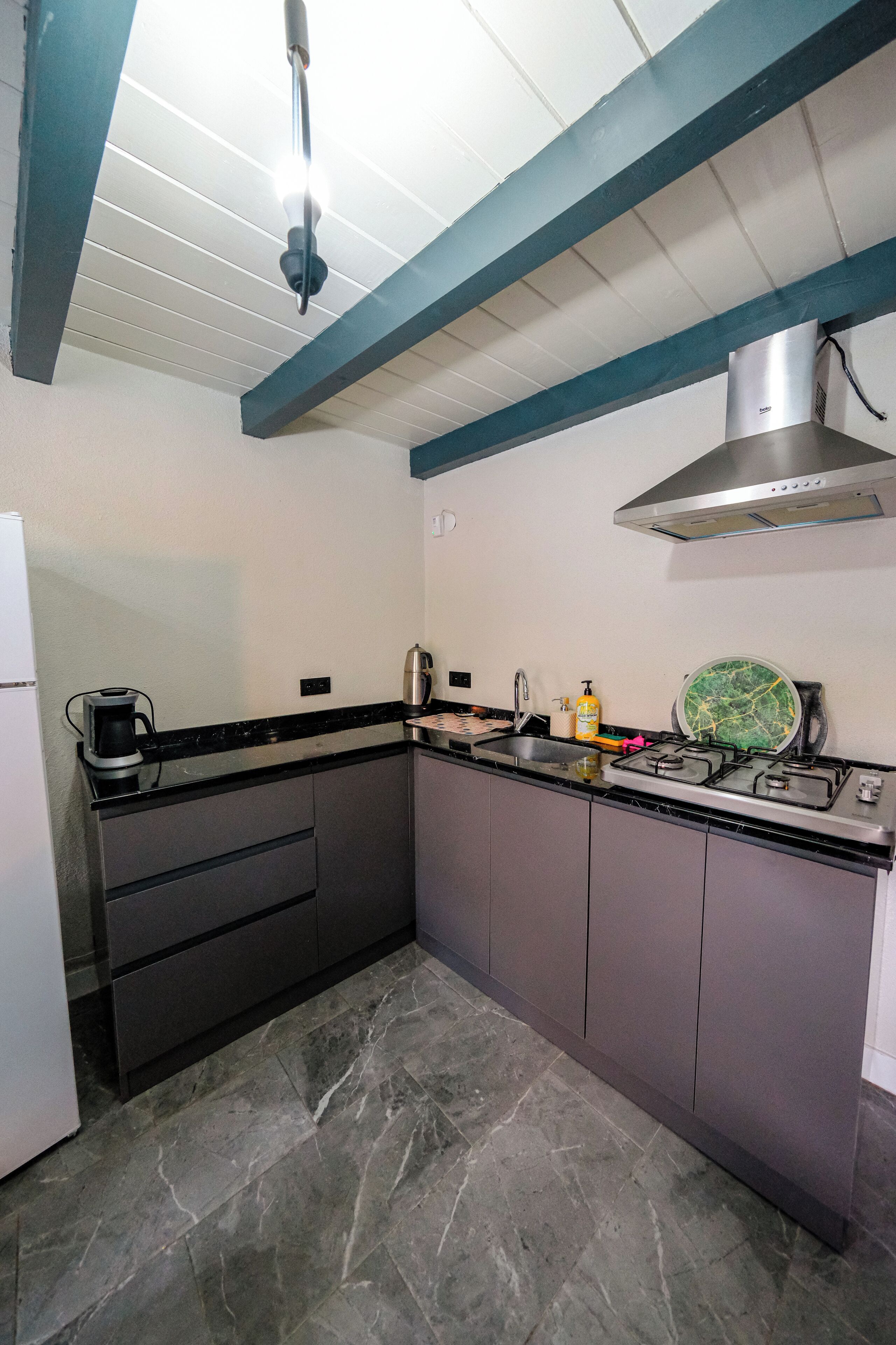 Una cocina compacta con estufa a gas, cafetera y pileta.
