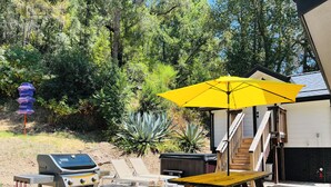 An outdoor deck with a grill, a wooden table, and a yellow umbrella.