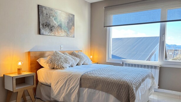A bedroom with a bed, bedside lamps, a window, and a painting on the wall. - Studio in Bariloche for two people (San Carlos de Bariloche)