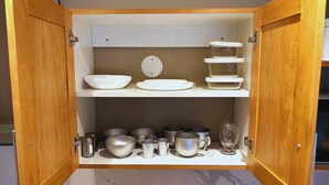 A wooden cabinet with shelves containing white bowls, plates, and various metal containers. - Studio in Bariloche for two people (San Carlos de Bariloche)