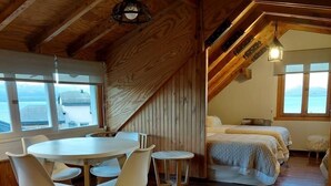 Un dormitorio acogedor en el ático, con techo de madera, un comedor con mesa y sillas redondas, y vista al mar a través de amplios ventanales.