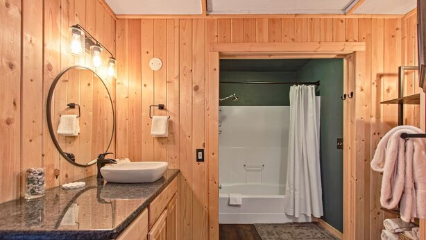 A wooden-paneled bathroom with a sink, mirror, and shower. - Amazing Lakefront Getaway-sleeps 18 guests, w/private dock, gameroom, spa & more (Hayden)