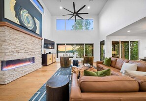 A spacious living room with a stone fireplace, leather sofa, and a large window overlooking a scenic view.